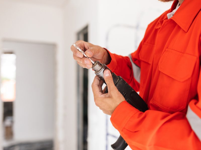 Close up builder in orange work clothes holding drill machine in